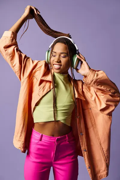 Happy african american young woman in headphones and vibrant casual attire on purple background — Stock Photo