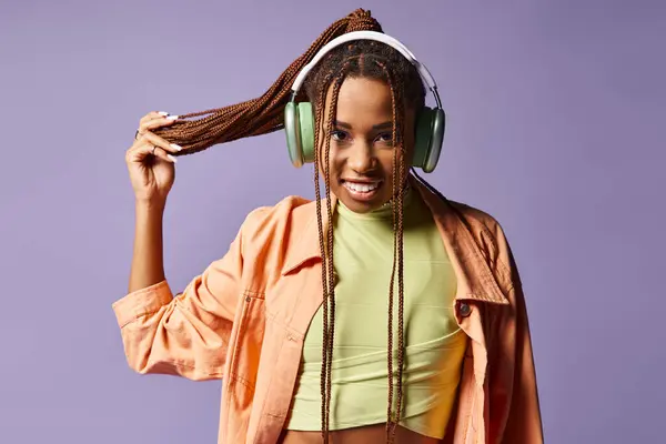 Happy african american young woman in headphones holding her dreadlocks on purple background — Stock Photo