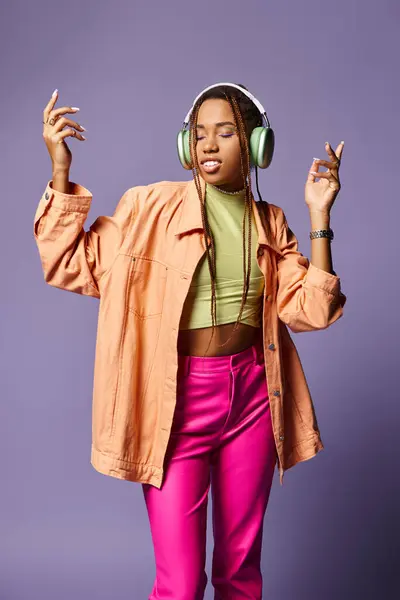 Ecstatic dance of happy african american girl in vibrant attire with headphones on purple backdrop — Stock Photo