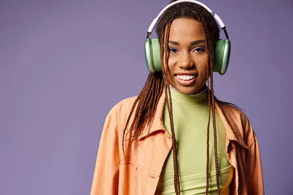 Positive african american woman in vibrant attire with wireless headphones on purple backdrop — Stock Photo