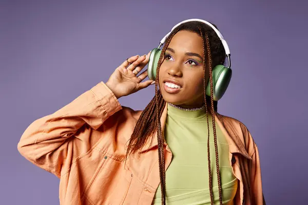 Happy african american woman in vibrant trendy attire with wireless headphones on purple backdrop — Stock Photo