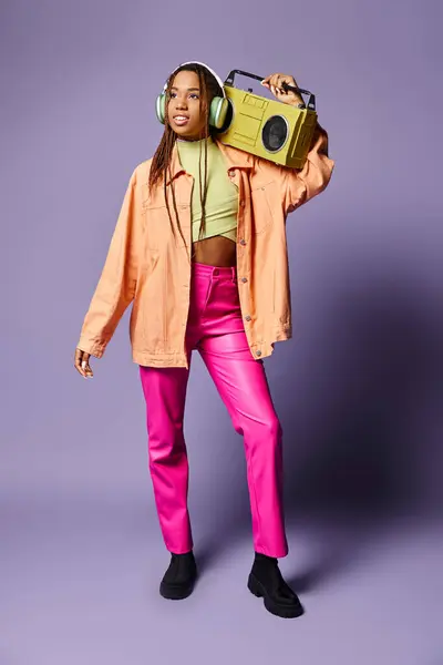 Heureux afro-américaine fille dans des écouteurs sans fil debout avec boombox rétro sur fond violet — Photo de stock