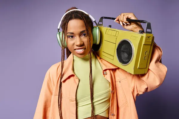 Щаслива афроамериканка в бездротових навушниках, що стоять з ретро бумбокс на фіолетовому тлі — стокове фото