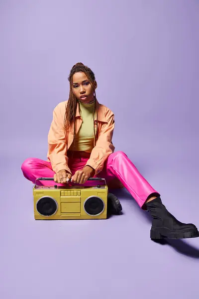 Stylish african american woman with dreadlocks sitting next to retro boombox on purple backdrop — Stock Photo