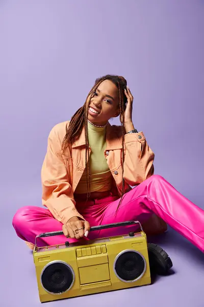 Happy african american woman with dreadlocks sitting next to retro boombox on purple backdrop — Stock Photo