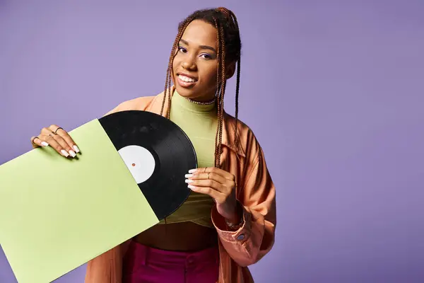 Happy young african american woman in her 20s with dreadlocks holding vinyl disc on purple backdrop — Stock Photo