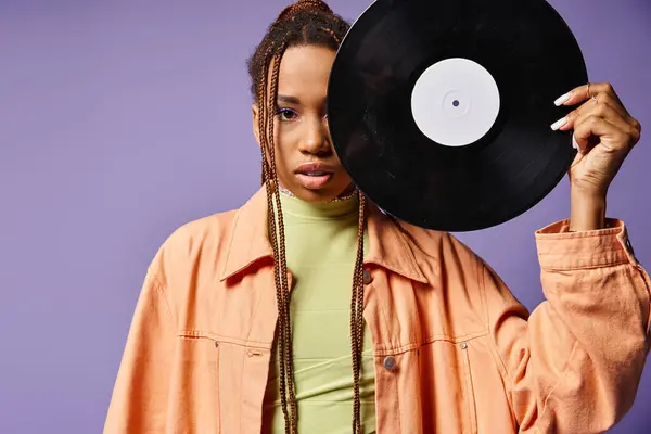 African american woman in her 20s with dreadlocks covering half of face with vinyl disc on purple — Stock Photo