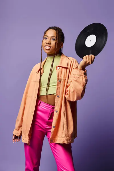 Happy young african american girl in her 20s with dreadlocks holding vinyl disc on purple backdrop — Stock Photo