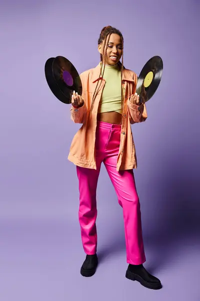 Happy african american girl in her 20s with dreadlocks comparing vinyl discs on purple backdrop — Stock Photo