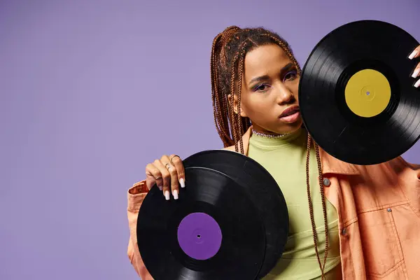 Junge afrikanisch-amerikanische Frau in ihren Zwanzigern mit Dreadlocks posiert mit Schallplatten vor lila Hintergrund — Stockfoto