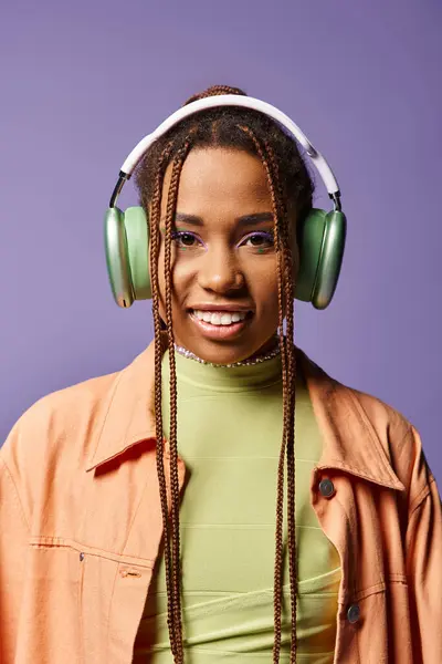 Jolly african american woman in vibrant attire with wireless headphones on purple backdrop — Stock Photo