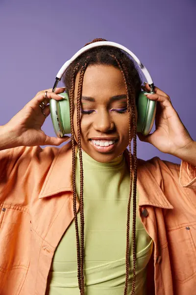 Joyeuse femme afro-américaine en tenue vibrante avec écouteurs sans fil sur fond violet — Photo de stock