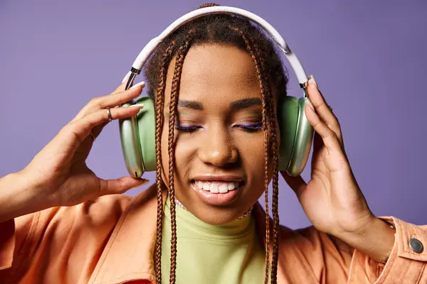 Jolie femme américaine africaine en tenue vibrante avec écouteurs sans fil sur fond violet — Photo de stock
