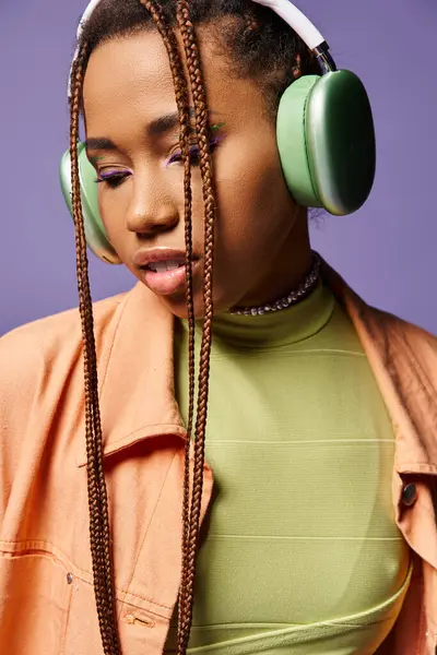 Pretty african american girl in 20s listening music in wireless headphones on purple backdrop — Stock Photo