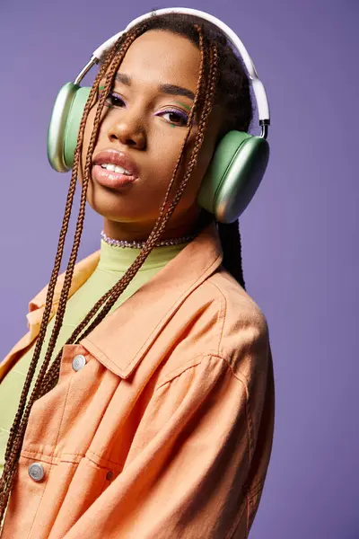 Pretty african american girl in 20s listening music in wireless headphones on purple background — Stock Photo