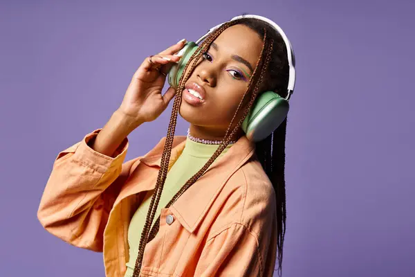 Pretty african american woman in 20s listening music in wireless headphones on purple background — Stock Photo