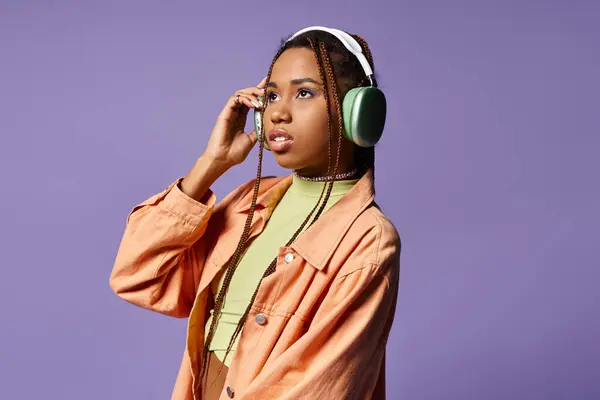Dreamy african american woman in 20s listening music in wireless headphones on purple background — Stock Photo