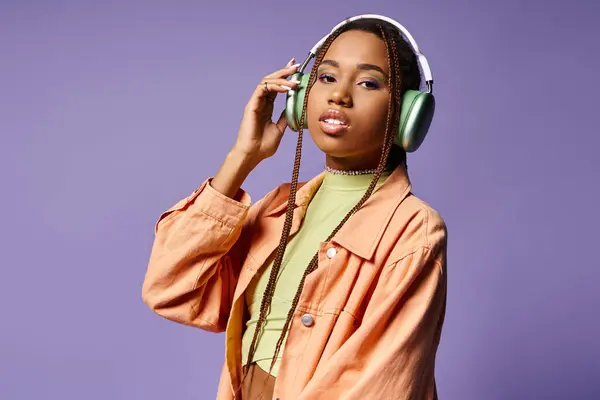 Alluring african american woman in 20s listening music in wireless headphones on purple background — Stock Photo