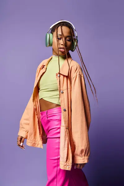 Alluring african american woman in 20s listening music in wireless headphones and walking on purple — Stock Photo
