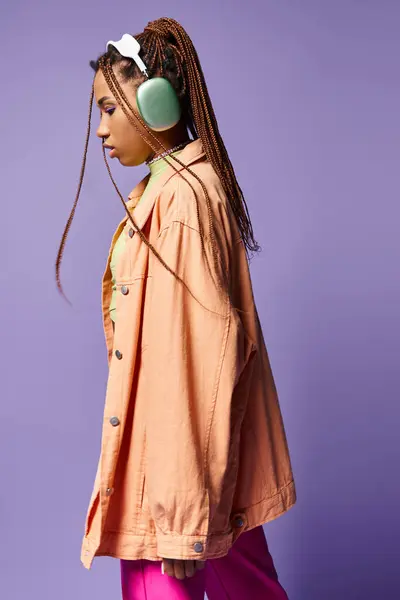 Vue de côté afro-américaine fille dans les années 20 écouter de la musique dans les écouteurs sans fil et marcher sur violet — Photo de stock