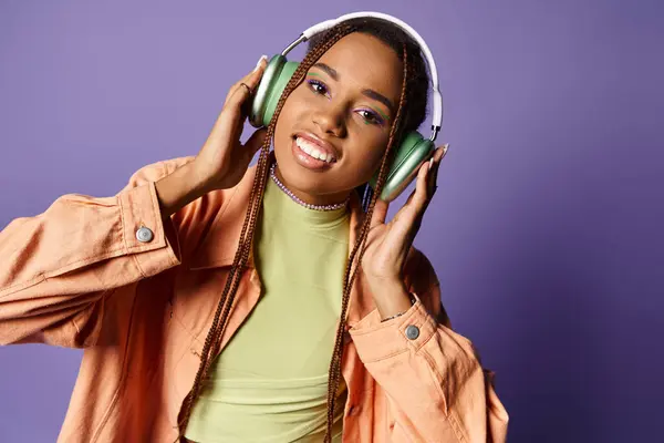 Pleased african american girl in 20s listening music in wireless headphones and looking at camera — Stock Photo