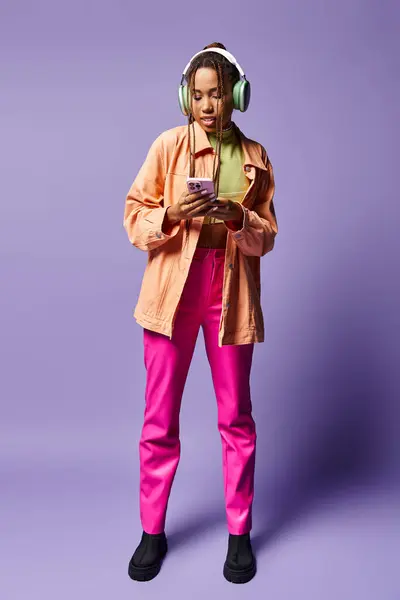 Feliz mulher afro-americana em seus fones de ouvido sem fio usando smartphone em pano de fundo lilás — Fotografia de Stock