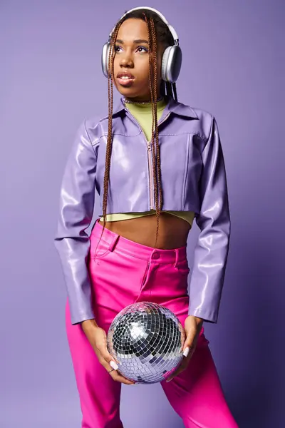 Giovane donna afroamericana in cuffie wireless alla moda che tiene palla disco su sfondo viola — Foto stock