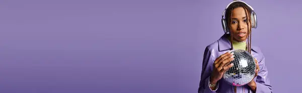 Jeune fille afro-américaine dans des écouteurs sans fil élégants tenant boule disco sur violet, bannière — Photo de stock