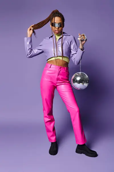 African american girl in futuristic sunglasses and headphones standing with disco ball on purple — Stock Photo