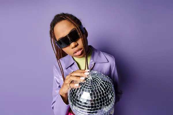 Portrait of african american woman in trendy sunglasses holding disco ball on on purple background — Stock Photo