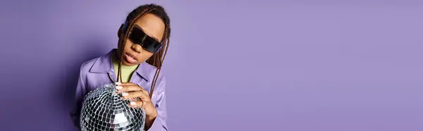 Pancarta de mujer afroamericana en gafas de sol de moda sosteniendo bola disco sobre fondo púrpura - foto de stock
