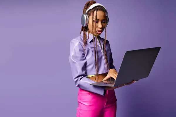 Focused african american woman with headphones working on laptop remotely on purple background — Stock Photo