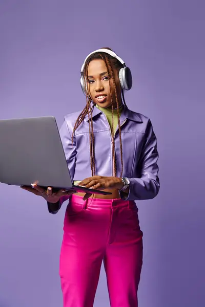 Junge afrikanisch-amerikanische Frau mit Kopfhörern, die auf dem Laptop ferngesteuert auf lila Hintergrund arbeitet — Stockfoto