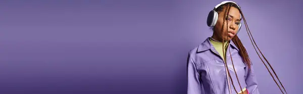 Афроамериканська дівчина з дредлоками і бездротовими навушниками насолоджується музикою на фіолетовому, банер — стокове фото