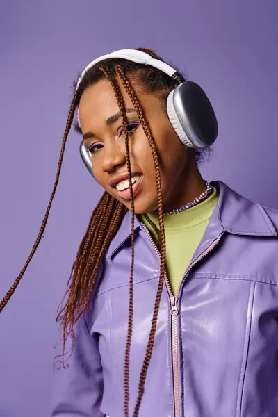 Sonriente joven afroamericana con auriculares inalámbricos disfrutando de música sobre fondo púrpura - foto de stock