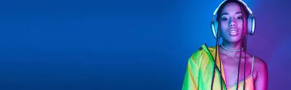 Horizontal banner of beautiful dark-skinned woman in headphones posing in studio with neon lights — Stock Photo