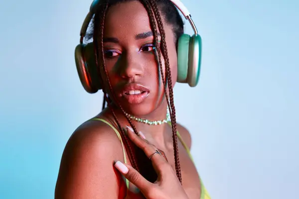 Verträumte afrikanisch-amerikanische Frau mit Dreadlocks in drahtlosen Kopfhörern schaut in die Kamera auf blau — Stockfoto