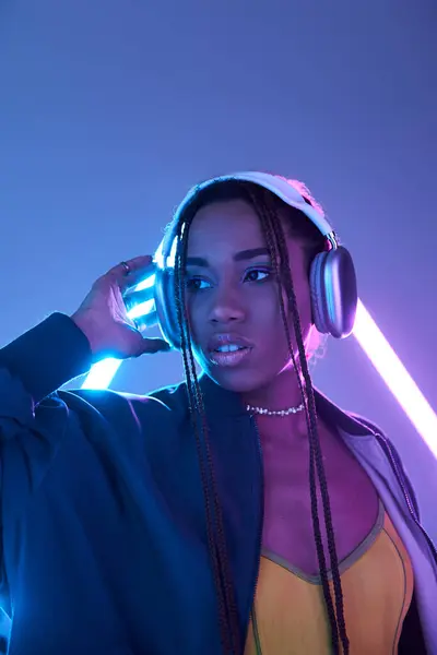 Stylish african american girl in dreadlocks and headphones in studio with blue fluorescent light — Stock Photo