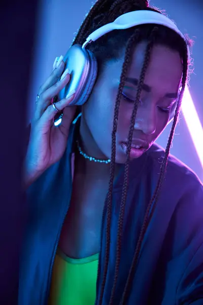 Pretty african american girl in headphones enjoying music in studio with fluorescent light — Stock Photo