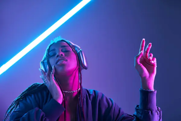 Ecstatic african american woman in headphones enjoying music in studio with fluorescent light — Stock Photo
