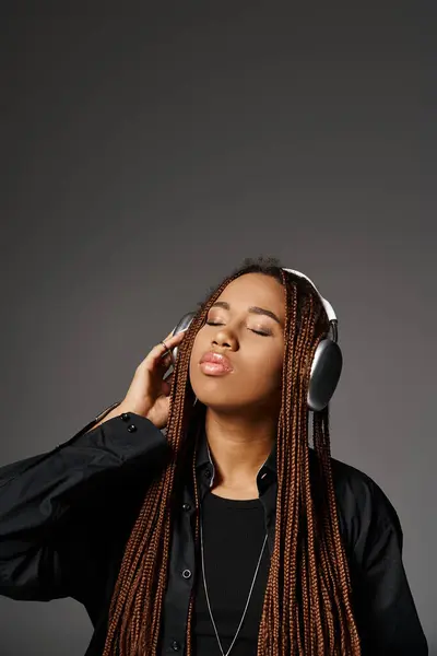 Young dark skinned woman with dreadlocks enjoying music in wireless headphones on grey backdrop — Stock Photo