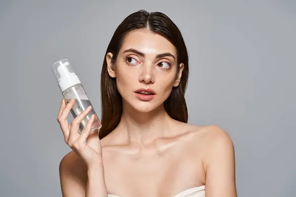 Eine junge kaukasische Frau mit brünetten Haaren hält eine Flasche mit Schaumreiniger vor ihr Gesicht und zeigt saubere Haut. — Stockfoto