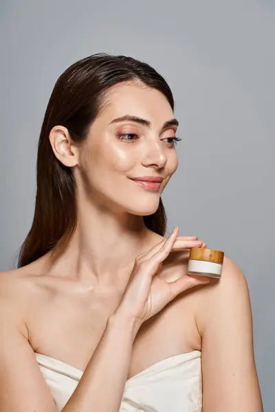 Una joven feliz mujer delicadamente sostiene un frasco de crema, exudando pureza y belleza. - foto de stock