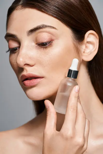 A young Caucasian woman with brunette hair and clean skin delicately holds a serum bottle of liquid in her hand. — Stock Photo