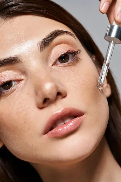 Close up de jovem caucasiana com olhos castanhos e pele limpa aplicando soro com pipeta cosmética — Fotografia de Stock
