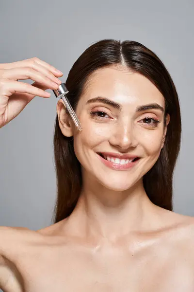 Une femme caucasienne heureuse avec des cheveux bruns et une peau propre appliquant du sérum avec une pipette cosmétique — Photo de stock