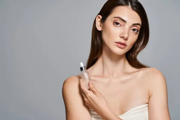 A young Caucasian woman gracefully holds a bottle with serum, exuding elegance and purity. — Stock Photo