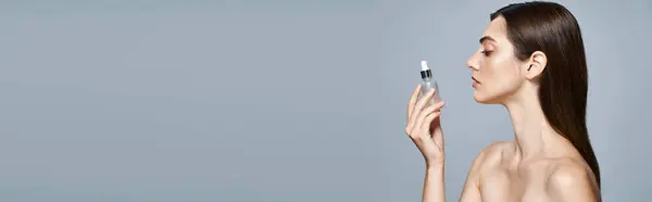 Jeune femme brune tenant un flacon avec du sérum, nourrissant sa peau dans un cadre studio, bannière — Photo de stock