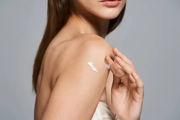 Молодая белая женщина с брюнетками и кремом на плече в студии. — стоковое фото