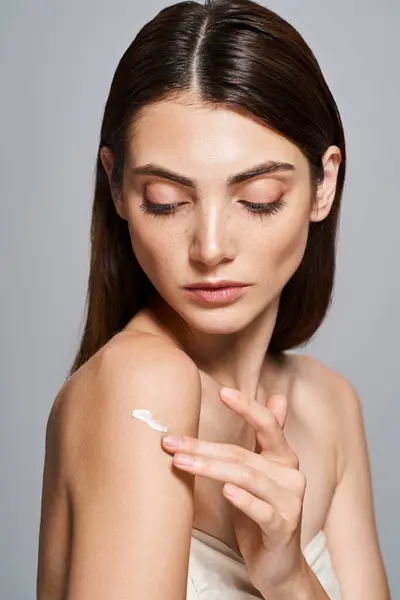 A young Caucasian woman with brunette hair gracefully applying cream on shoulder — Stock Photo